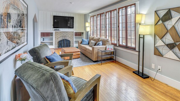 A spacious living room with a fireplace, a large window with multiple panes, and a modern art piece on the wall. - Lakeside Clifton Heights Home Near Forest Park (St. Louis)