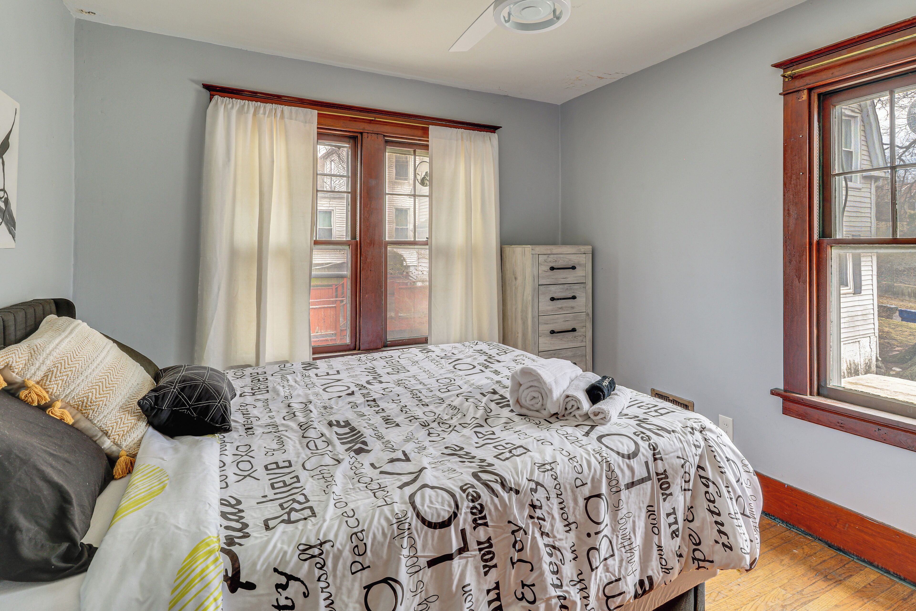 Een slaapkamer met een bed, een dressoir, een raam en een plafondventilator.