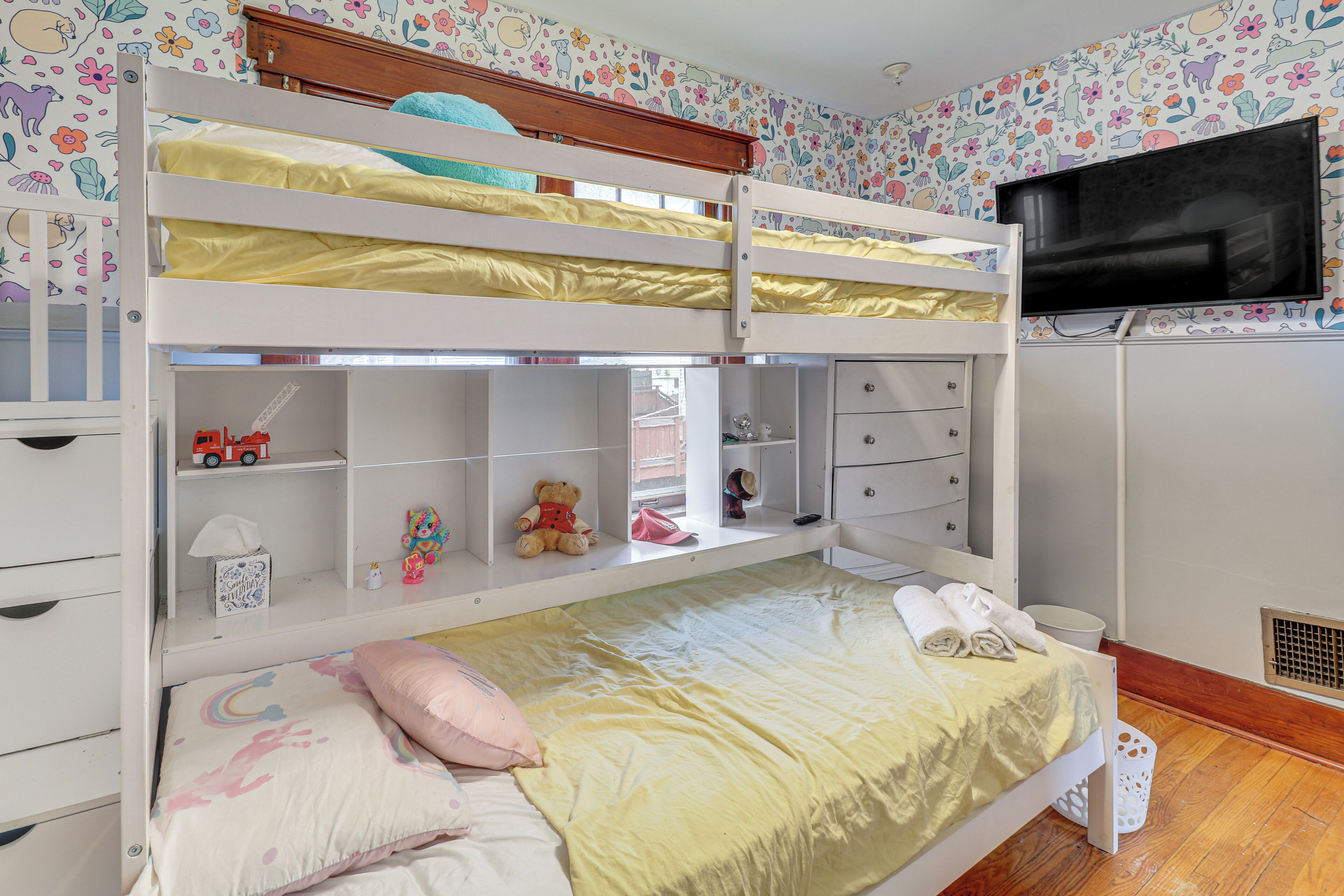 Une chambre avec un lit superposé, une télévision, des tiroirs de rangement et une fenêtre.