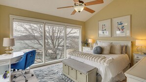 Ein Schlafzimmer mit großem Fenster, einem Bett, einem Schreibtisch und einem Deckenventilator.