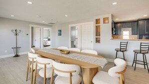 A modern kitchen with dark cabinetry, a wooden dining table with white chairs, and a small bar area.