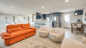 A modern living room with a sofa, two armchairs, a kitchen area with a microwave, and a dining area with a table and chairs.