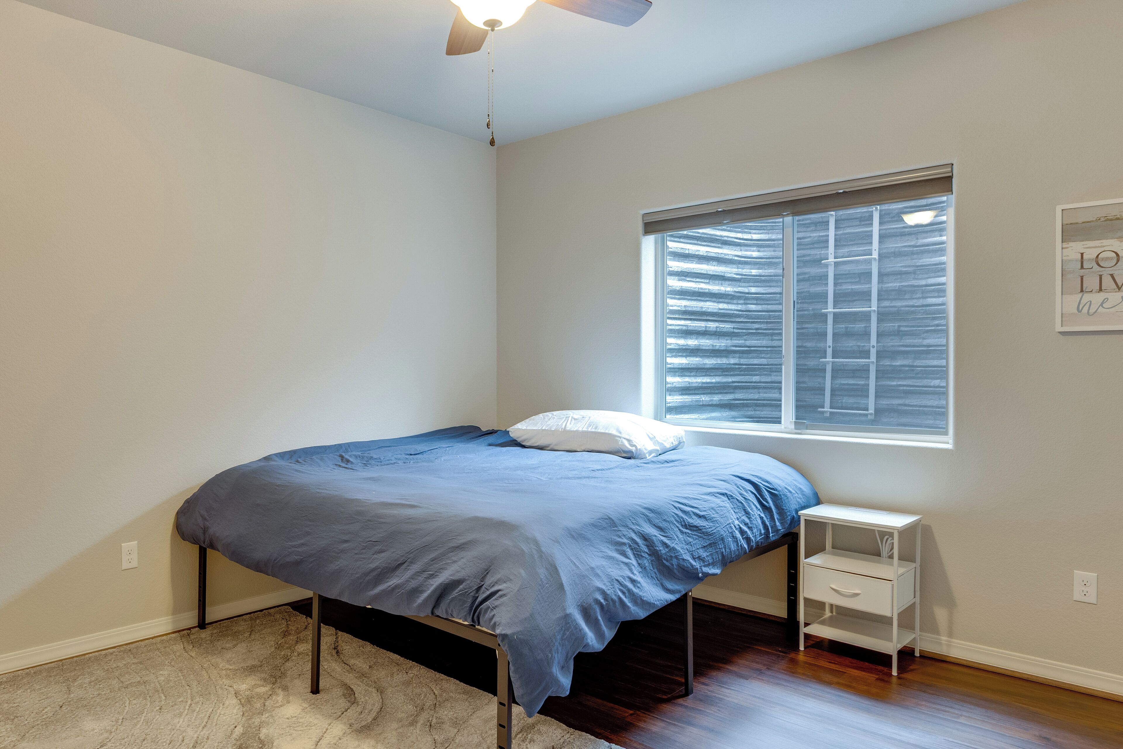 A bedroom with a bed, a nightstand, a window with blinds, and a ceiling fan.