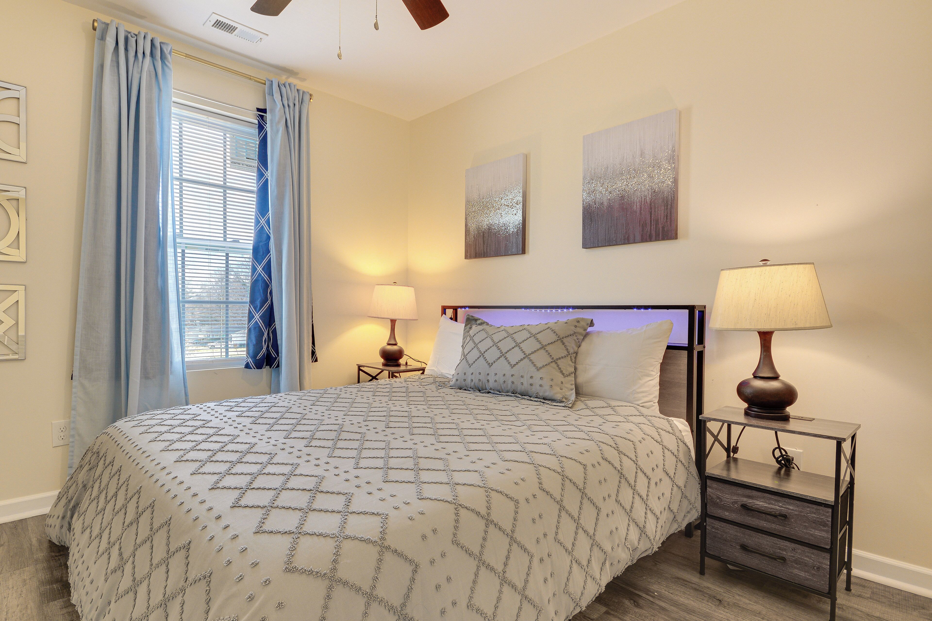 A bedroom with a bed, two bedside lamps, a nightstand, and a window with curtains.