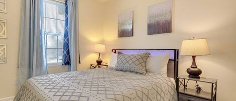 A bedroom with a bed, two bedside lamps, a nightstand, and a window with curtains.