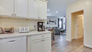 A kitchen with white cabinets, a dishwasher, a toaster, and a coffee maker. There is a dining area with a table and chairs in the background. - 1 Mi to Downtown Greensboro: Newly Built Home! (Greensboro)