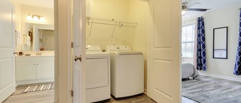 A laundry room with two front-loading washers and dryers, a drying rack, and a large window with curtains.