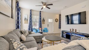 A living room with a sectional sofa, a round coffee table, a TV on a stand, and a ceiling fan. - 1 Mi to Downtown Greensboro: Newly Built Home! (Greensboro)