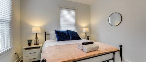 A neatly arranged bedroom with a bed, bedside lamps, a small table, and a window with blinds.