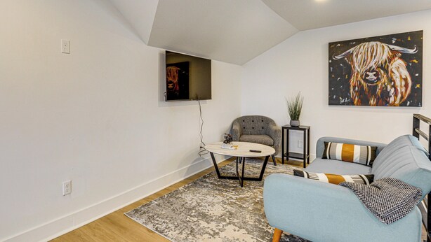 Un salon moderne avec un canapé, une table basse et un fauteuil. Un tableau est accroché au mur, et une petite table porte une plante.