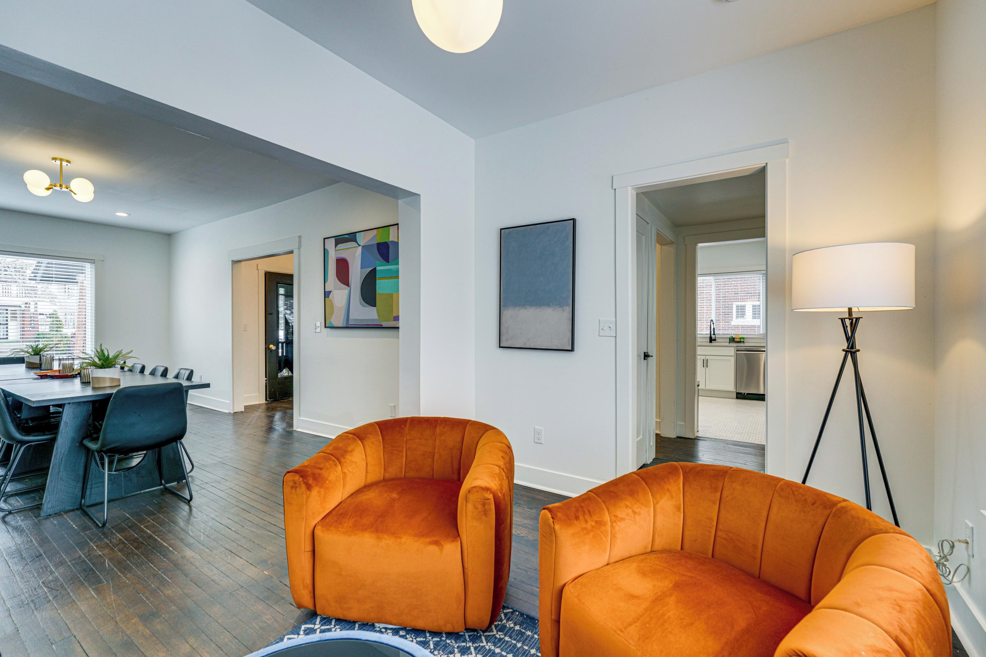 Een ruime woonkamer met een eethoek, met een groot raam, een vloerlamp en een modern abstract schilderij.