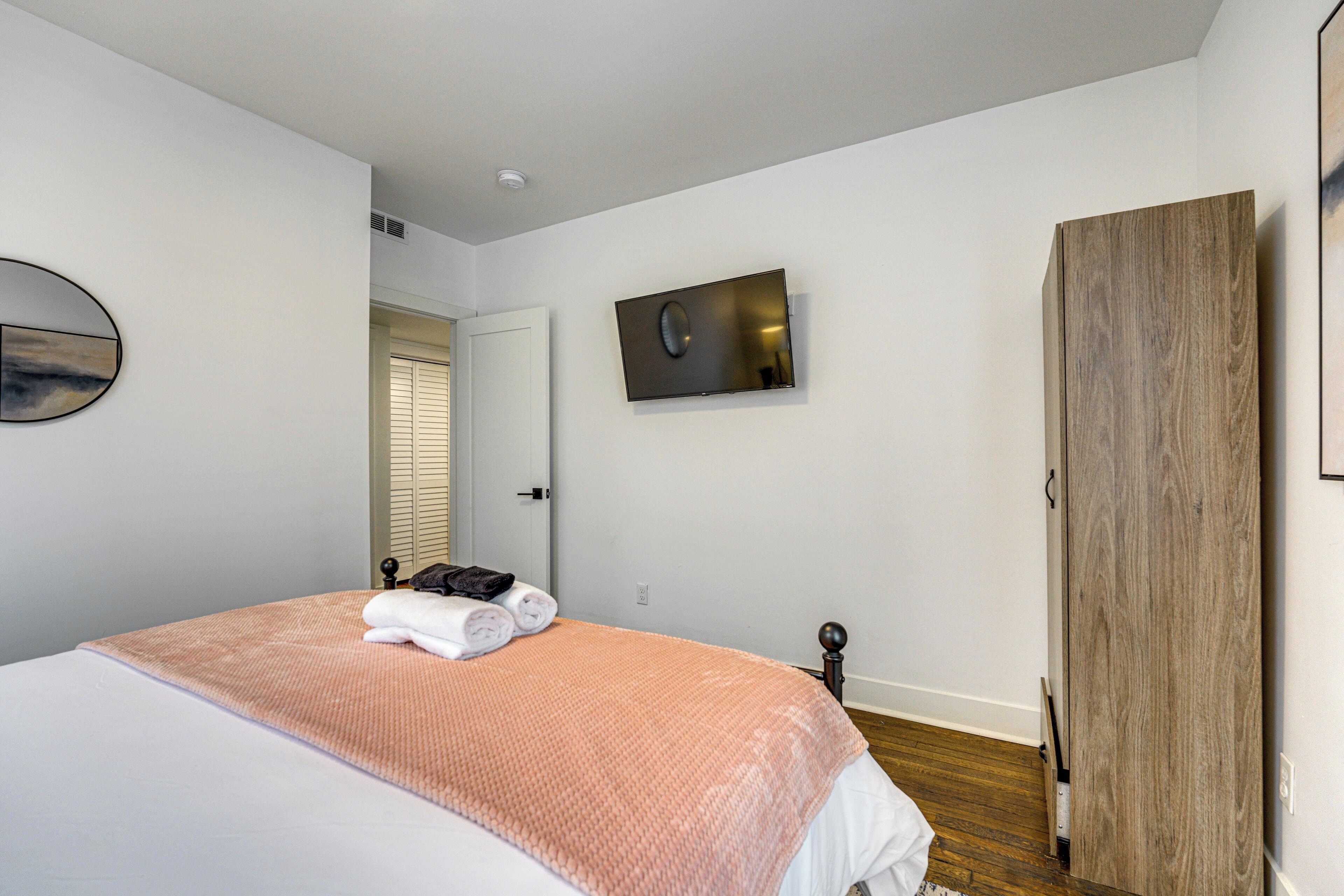 Un dormitorio con una cama, un televisor montado en la pared y un armario de madera.