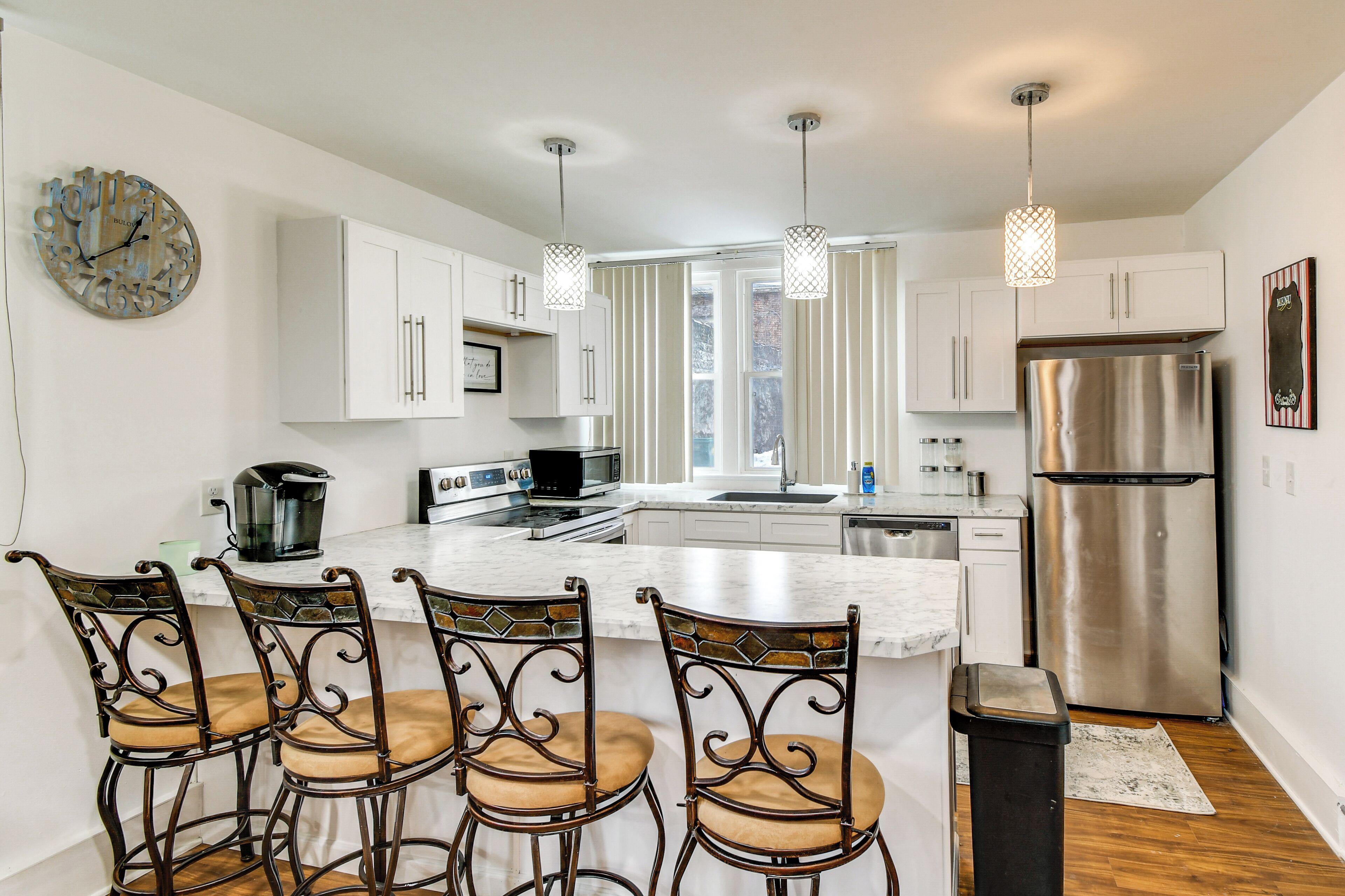 A modern kitchen with white cabinets, a stainless steel refrigerator, a large island with bar stools, and pendant lighting.