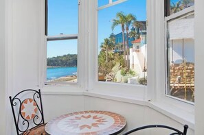 A room with a view of the sea and a patio area with a table and chairs.