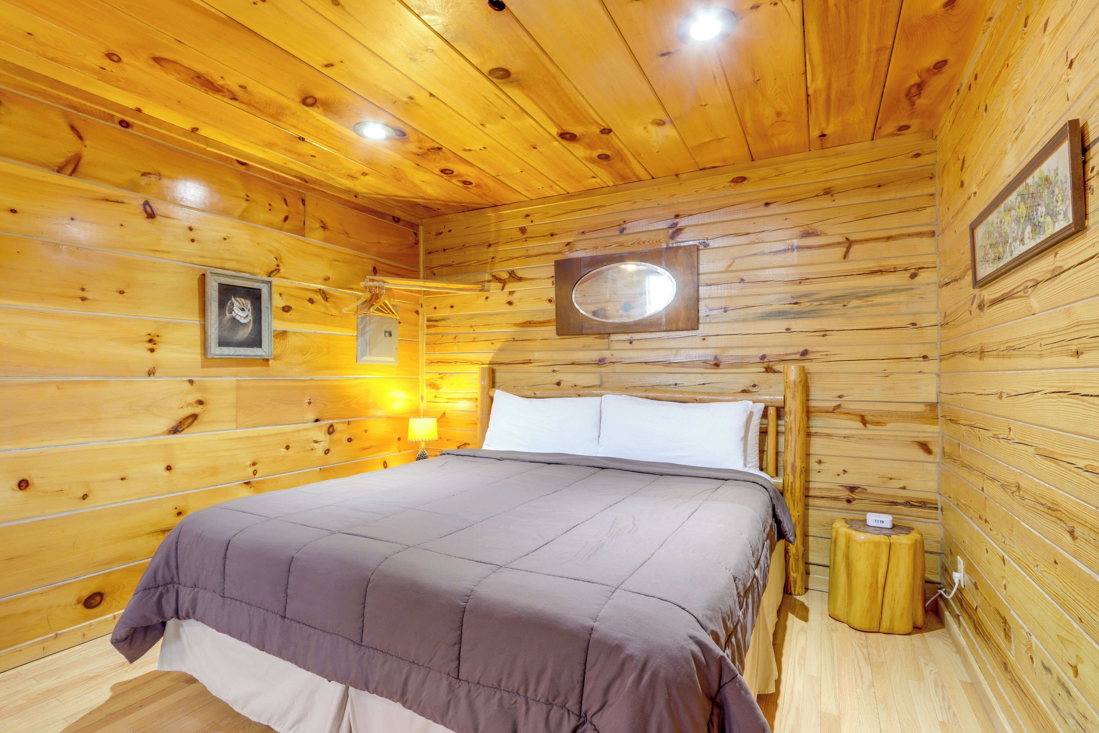 A wooden cabin room with a bed, a nightstand, a mirror, and a framed picture on the wall.