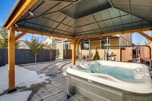 Ein Whirlpool unter einer überdachten Terrasse mit einer Holzkonstruktion und Blick auf einen Garten.