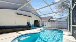 En pool med tak, ett solskydd, en sittplats och utsikt över trädgården.