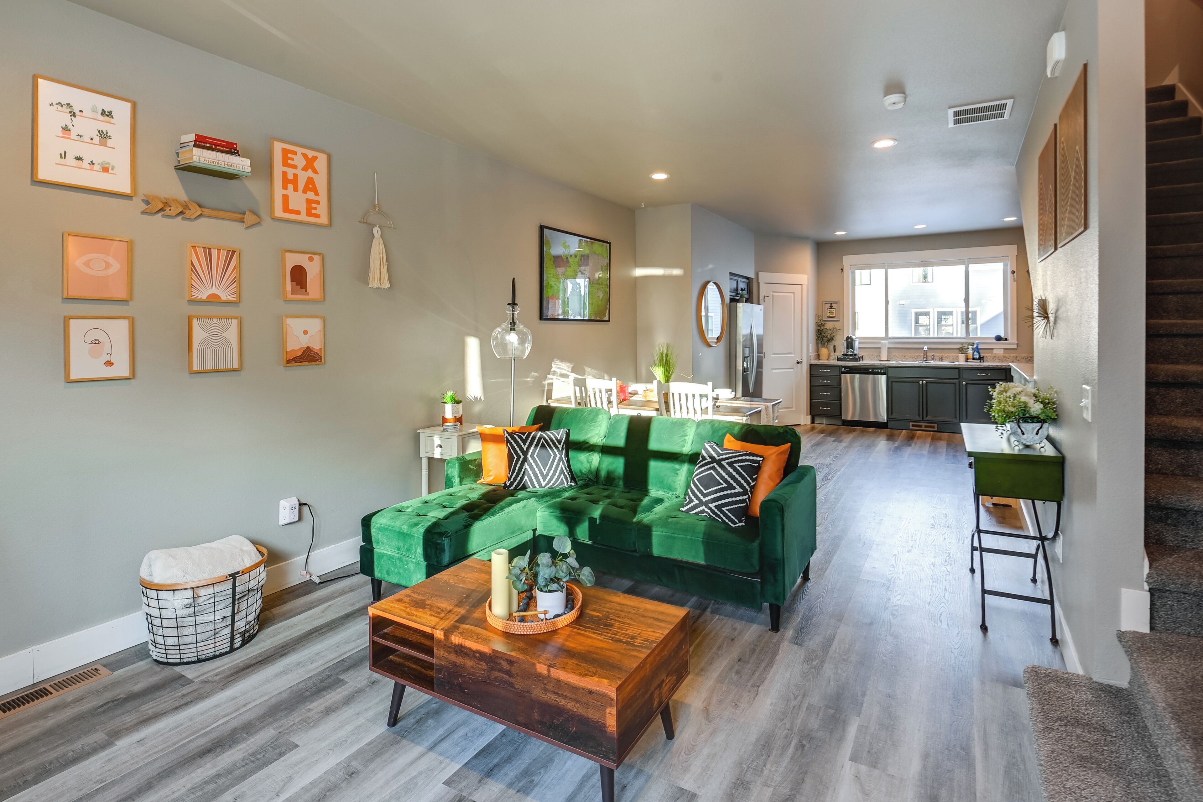 Een moderne woonkamer met een groene bank, een houten salontafel en een keuken op de achtergrond.