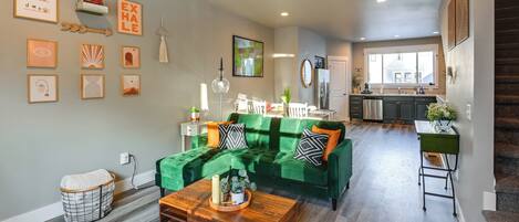 Een moderne woonkamer met een groene bank, een houten salontafel en een keuken op de achtergrond.