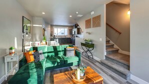 Un salon avec un canapé vert, une table basse et un escalier menant à la cuisine.