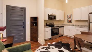 A compact kitchen with white cabinets, a microwave, stove, and refrigerator. There's a dining table with chairs and a cowhide rug.