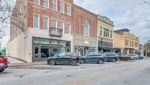 A street view with parked cars and a row of buildings with storefronts.