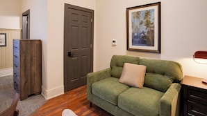 A room with a green sofa, a wooden dresser, a door, and a framed picture on the wall.