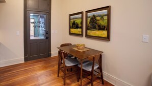 Een eetgedeelte met een houten tafel en vier stoelen, een donker houten deur en twee landschapsschilderijen aan de muur.