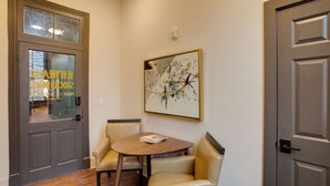 Un hall d’hôtel avec une table en bois et deux fauteuils en cuir, un tableau abstrait encadré accroché au mur, et une porte dotée d’un panneau en verre.