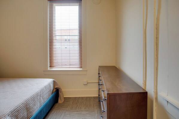 Un dormitorio con cama, cómoda, ventana con persianas y piso alfombrado.
