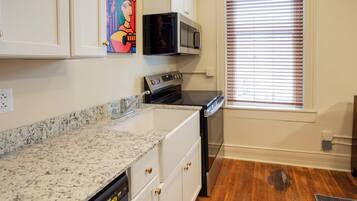 A kitchen with white cabinets, a granite countertop, a microwave, an oven, and a window with blinds.