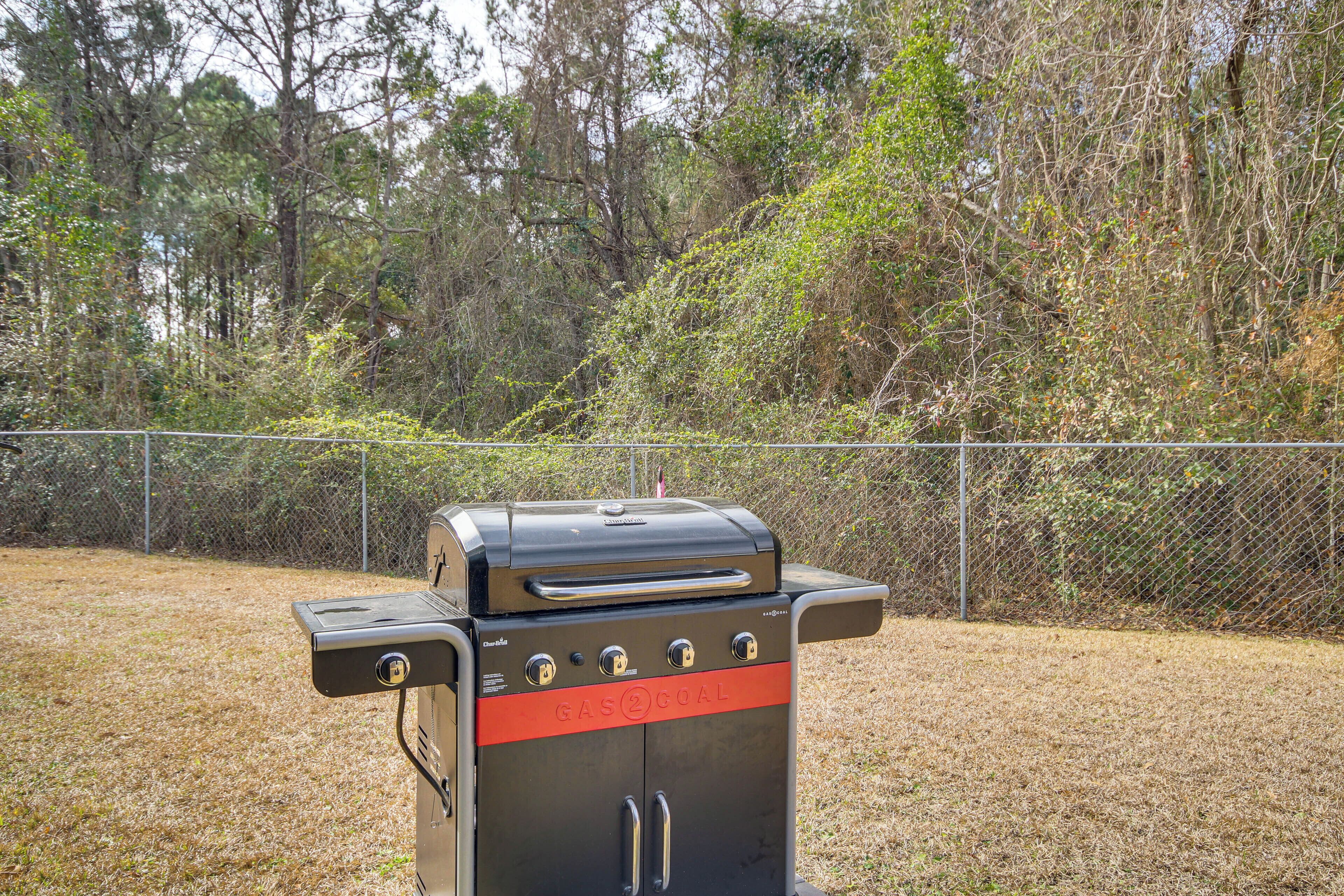 Una parrilla de gas portátil con pantalla digital y varios mandos, frente a un jardín vallado con árboles.