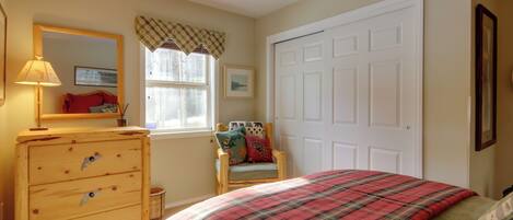 A bedroom with a bed, dresser, chair, window, and door.