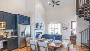 A modern kitchen with dark blue cabinets, a stainless steel refrigerator, and a dining area with a wooden table and chairs. - The Hideaway at Lake Greenwood Marina Access (Greenwood)