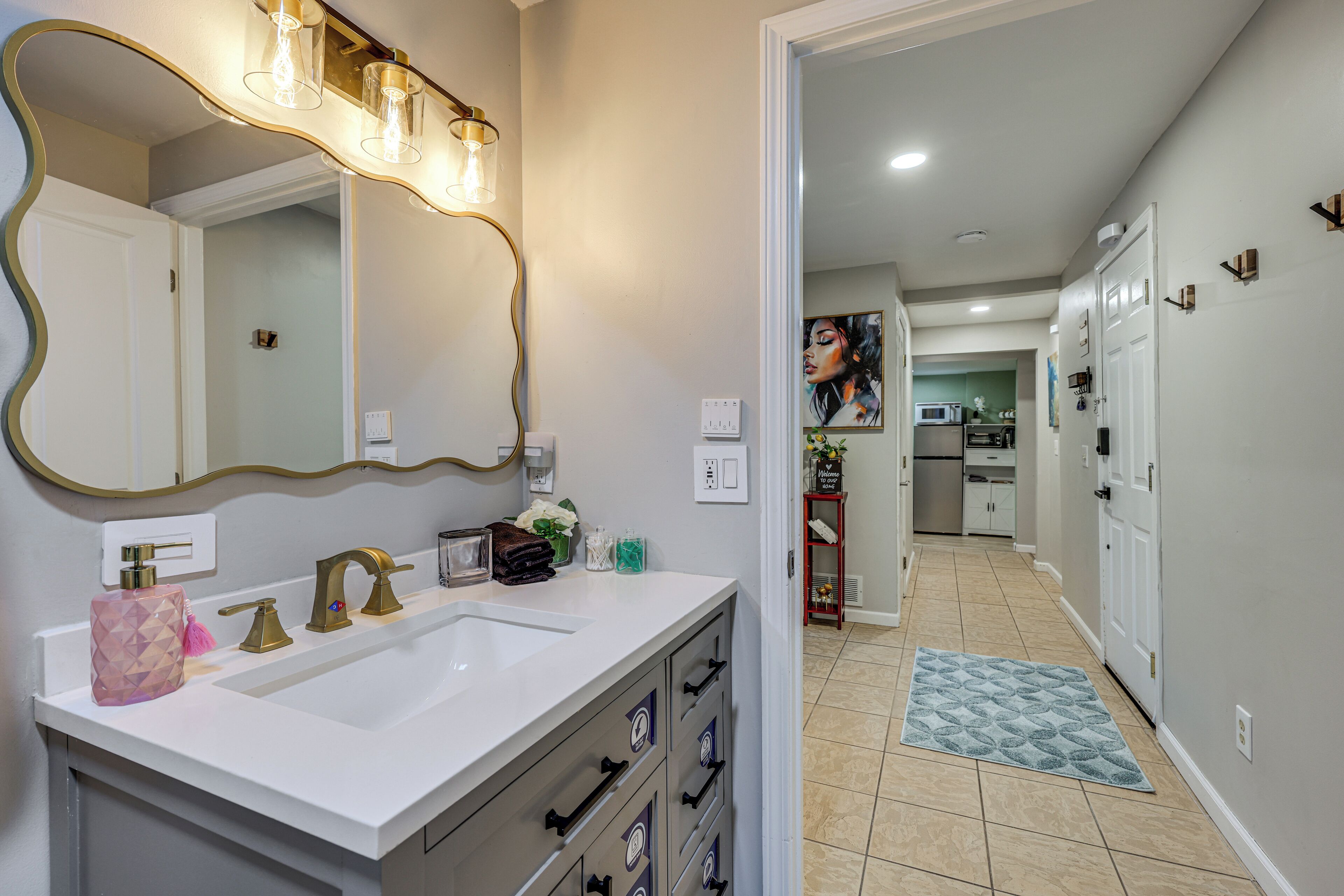 A bathroom with a white sink, gold fixtures, and a large mirror with lights.