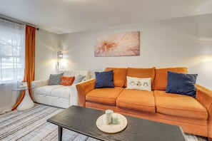 A living room with a white sofa, an orange sofa, a coffee table with candles, and a wall-mounted lamp.