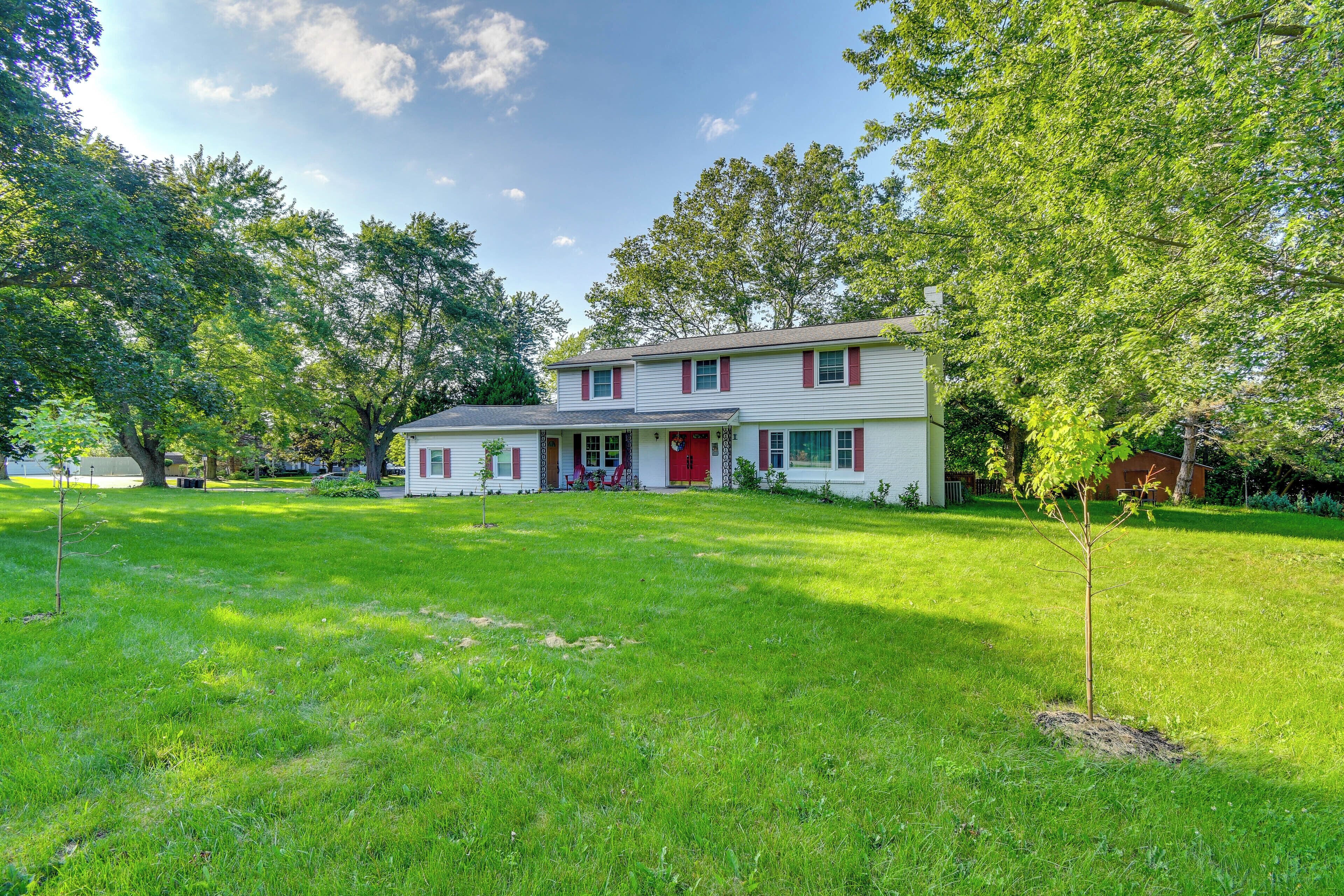 A two-story house with a front porch and a red door, surrounded by a well-maintained lawn and trees.