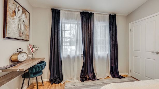 Een slaapkamer met een bed, een bureau met stoel, een klok en een raam met gordijnen.