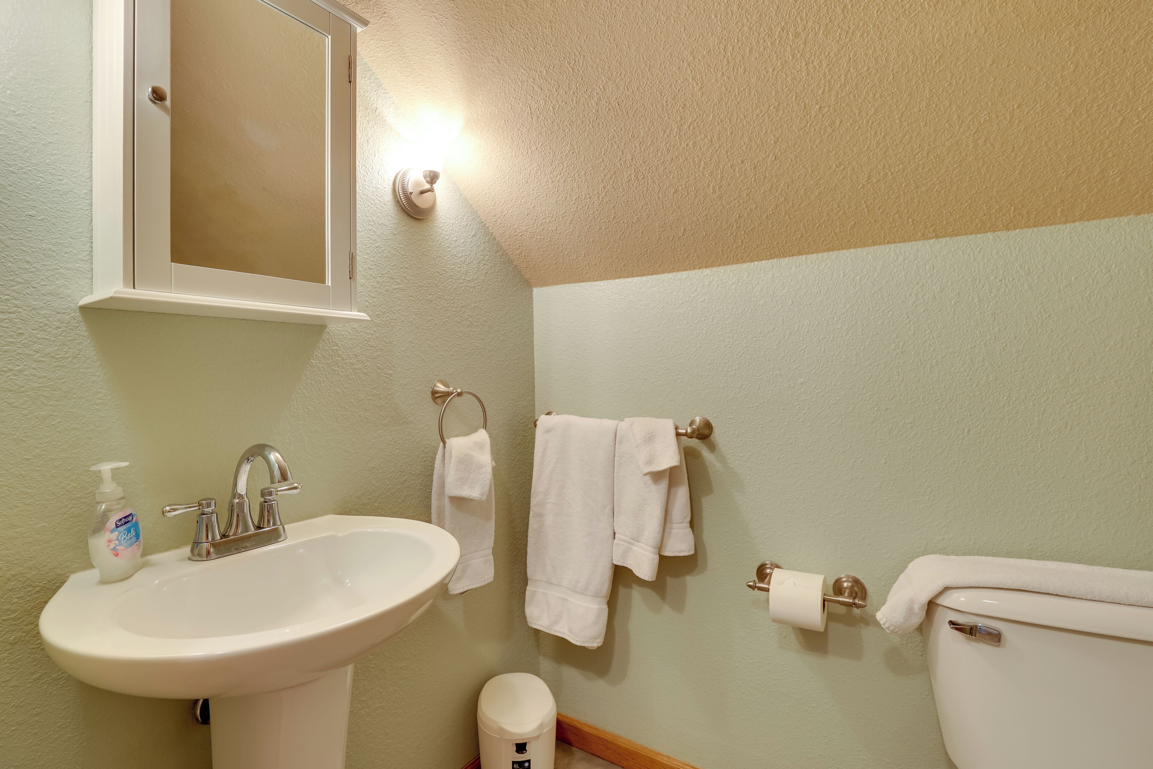 A bathroom with a sink, mirror, towel rack, toilet, and a soap dispenser.
