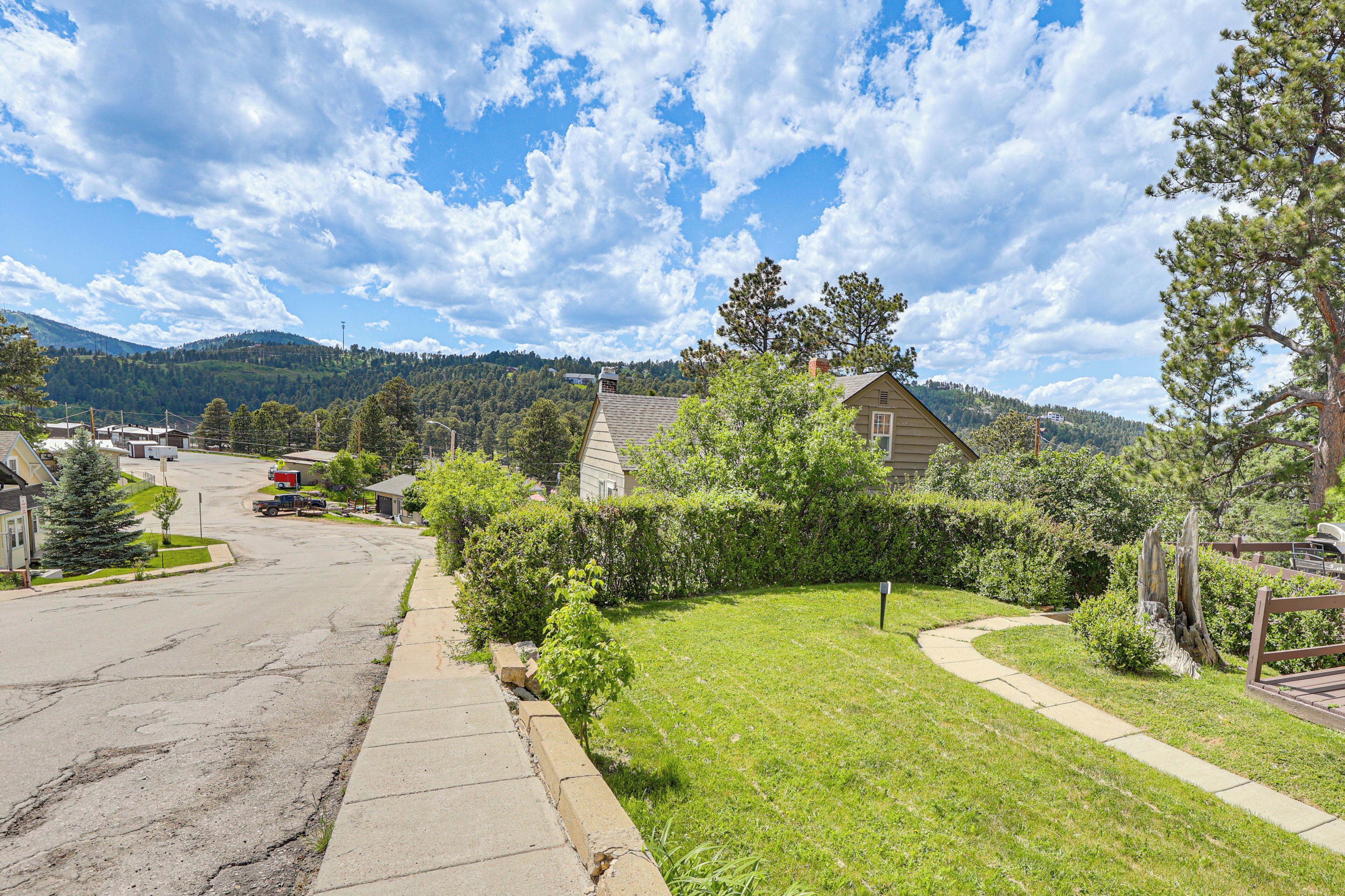 A residential street with houses, a clear sky, and a hilly landscape in the background.