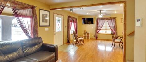 A living room with a leather sofa, wooden flooring, and a TV mounted on the wall.