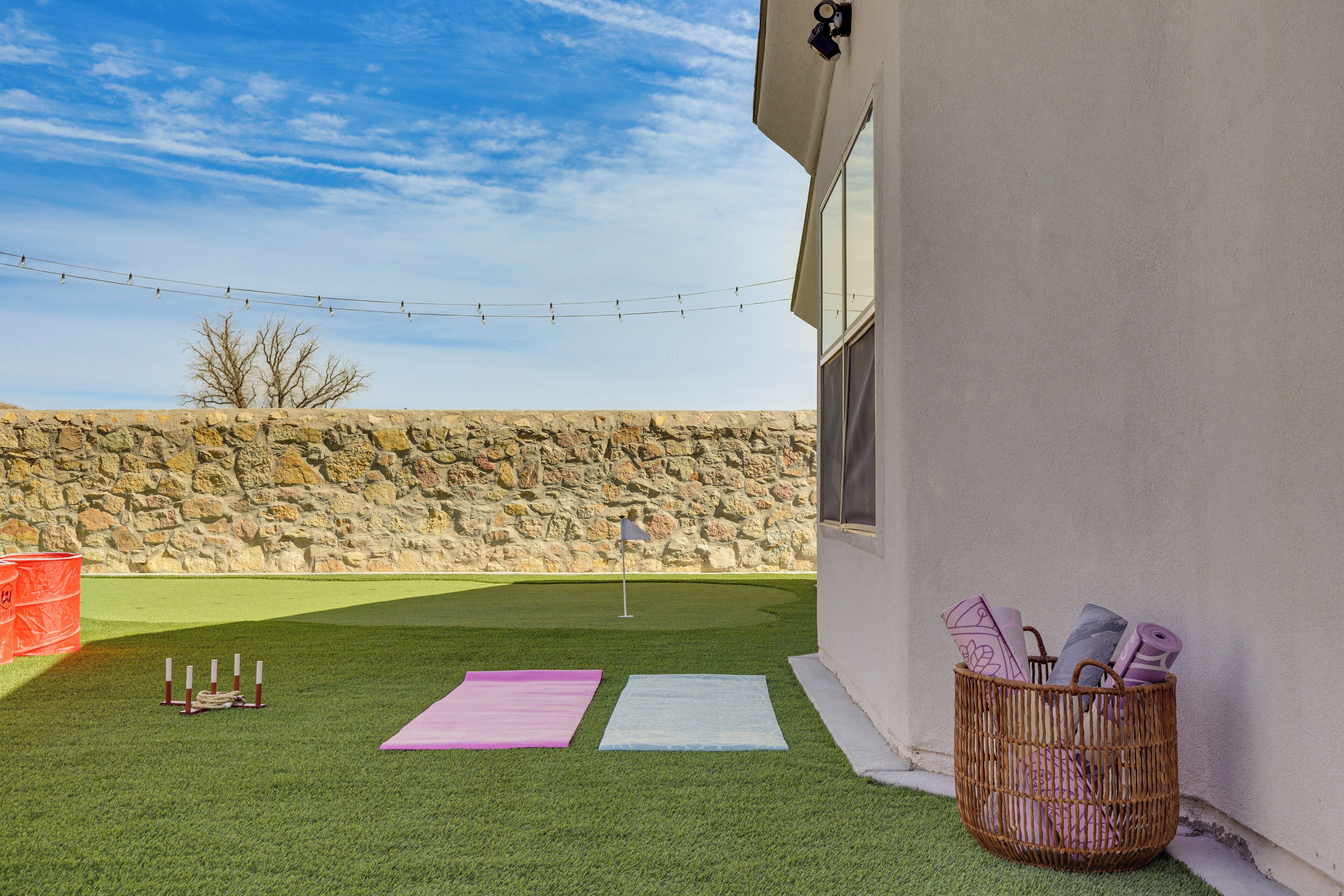 A backyard with artificial grass, a stone wall, and a basket of yoga mats.