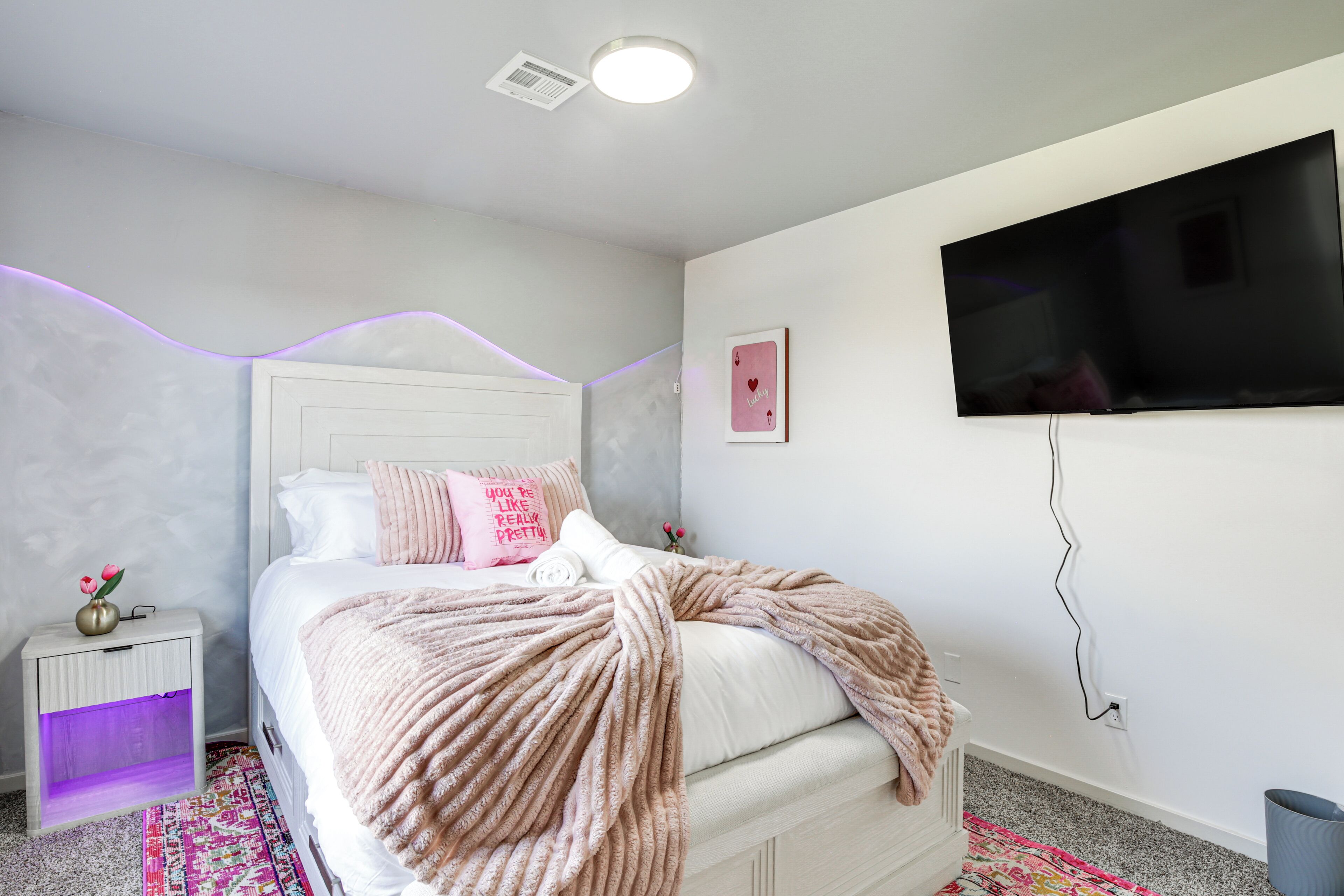Quarto com cama, mesa de cabeceira, televisão e tomada na parede.