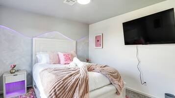 Quarto com cama, mesa de cabeceira, televisão e tomada na parede.