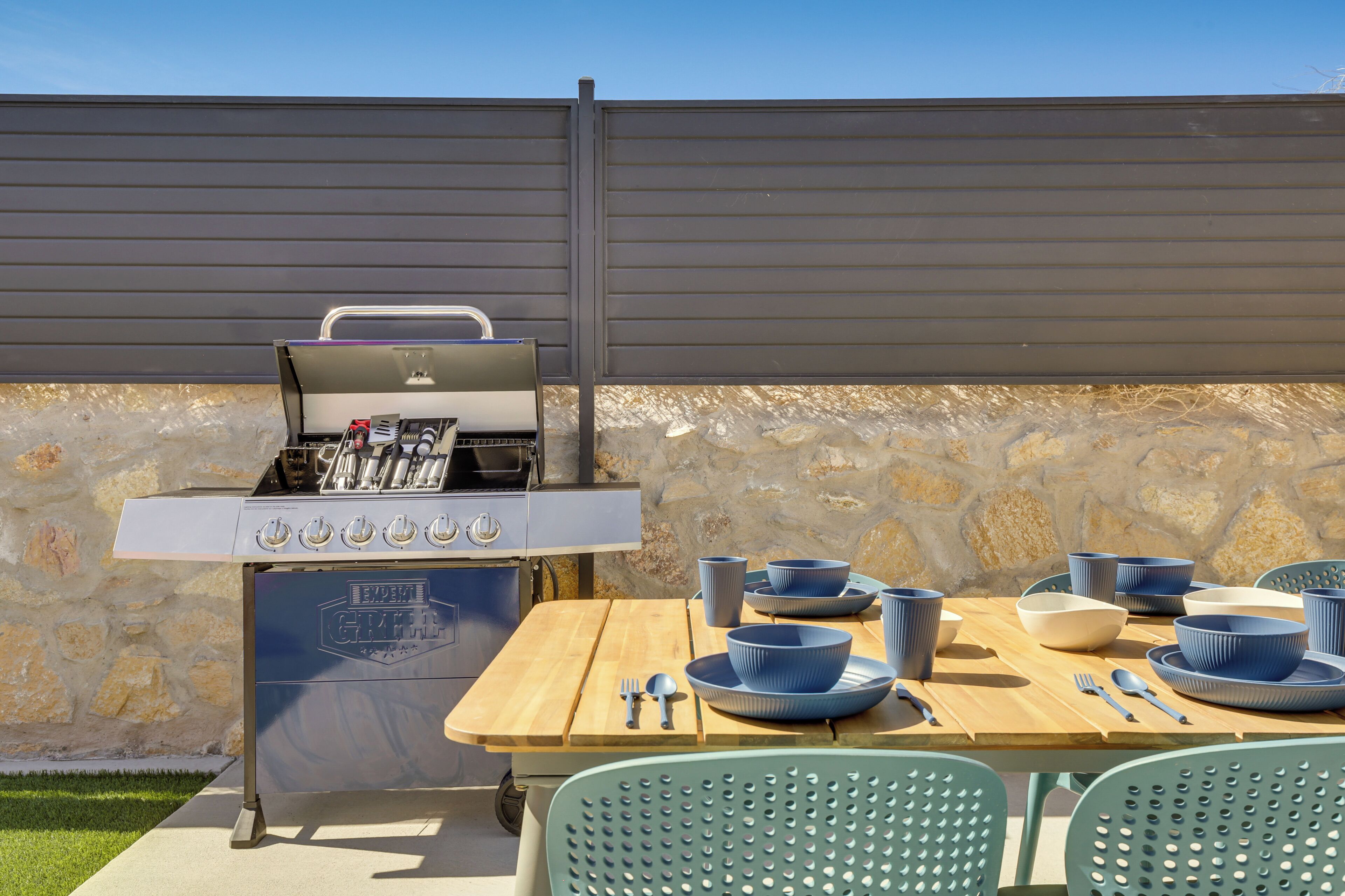 Ein Grillplatz im Freien mit Grill, Esstisch und blauem Geschirr.
