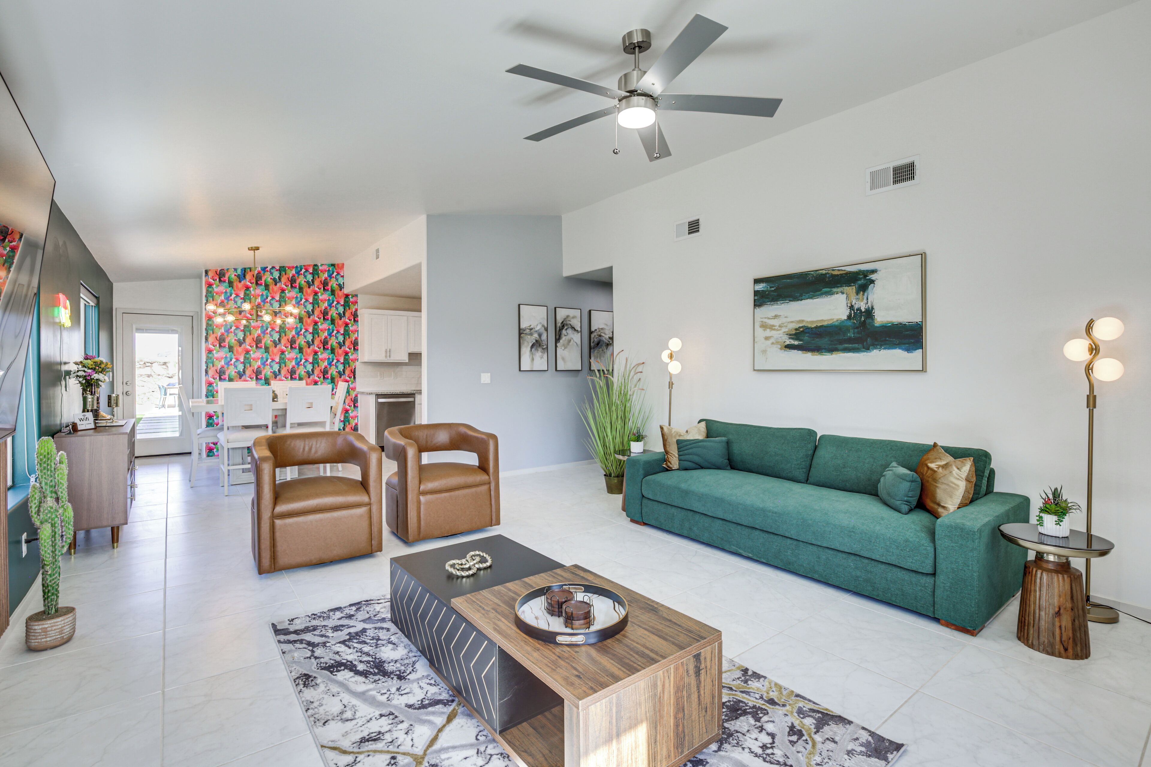 A modern living room with a green sofa, leather armchairs, a coffee table, and a ceiling fan.