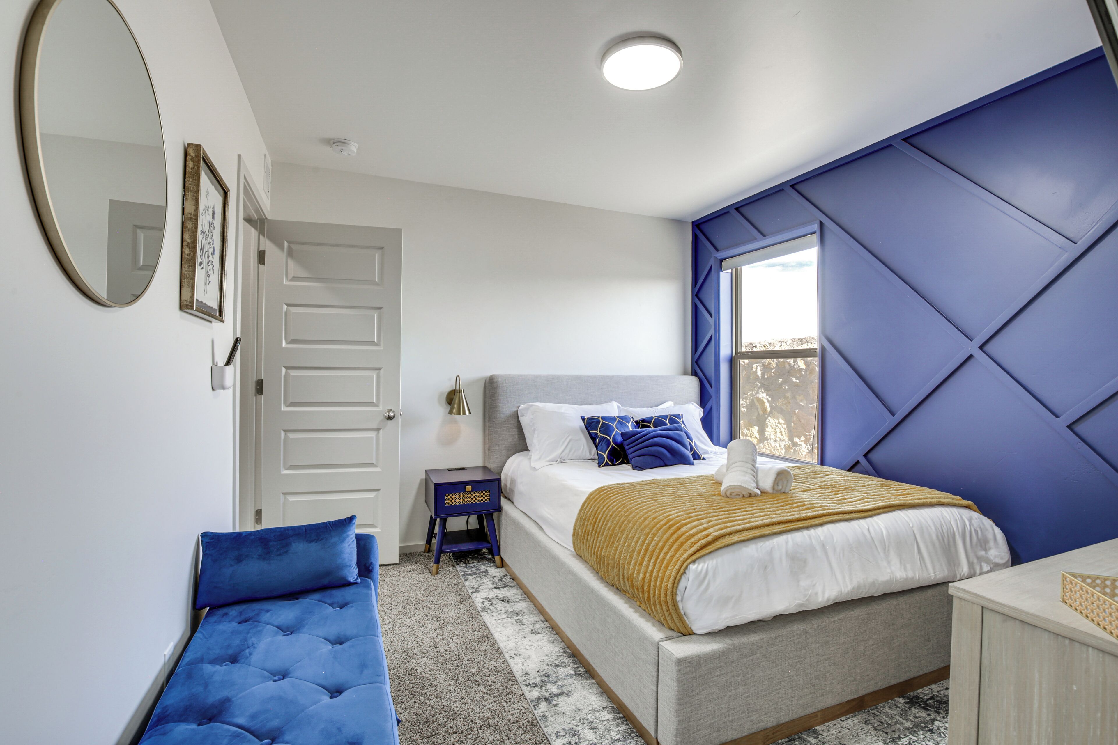 A bedroom with a bed, a bench, a dresser, a mirror, and a window.