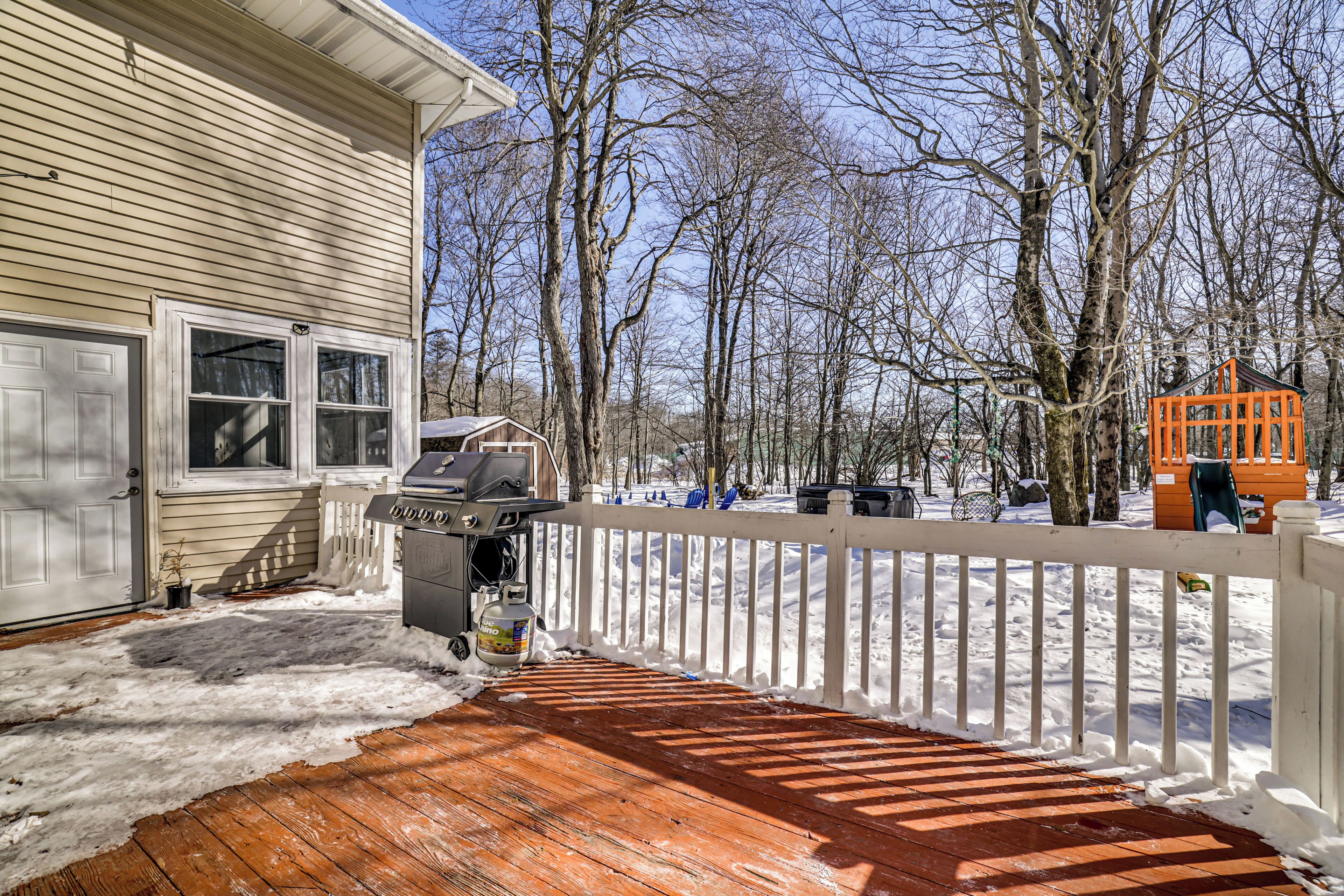 A wooden deck with a white railing, a barbecue grill, and a small shed in a snowy outdoor area.