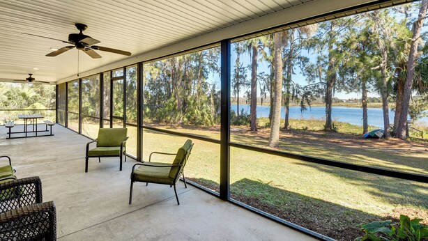 Un patio couvert doté de grandes fenêtres, de mobilier d’extérieur et d’un ventilateur de plafond.