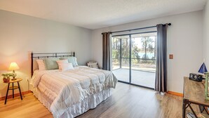 Une chambre avec un grand lit, une table de chevet, une lampe et une vue à travers une porte vitrée.